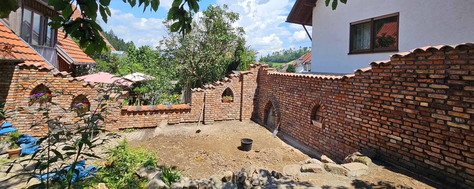 Umbau eines Gartens mit dekorativer Backsteinmauer, Blumenarrangements und sonnigem Wetter.