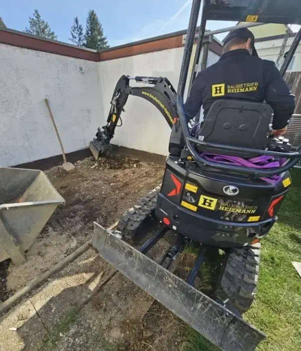 Mini-Bagger von Bauunternehmung aktiv beim Aushub auf engem Raum neben einer Hauswand, für präzise Bauarbeiten geeignet.