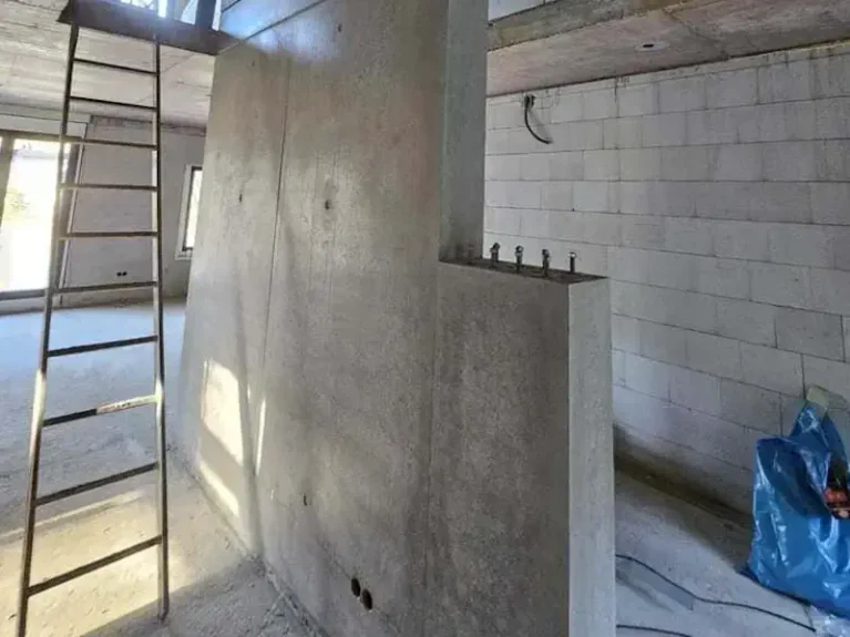 Unfertiger Innenraum: Betontreppe in Bau, Leiter stützt Zugang. Baustelle mit Wänden und Rohbau.