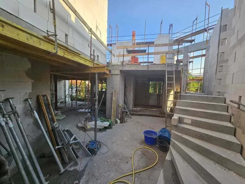 Baustelle mit Rohbau, Gerüsten und Baumaterialien, sonniger Tag, Fortschritt beim Hausbau sichtbar, Arbeit in vollem Gange.