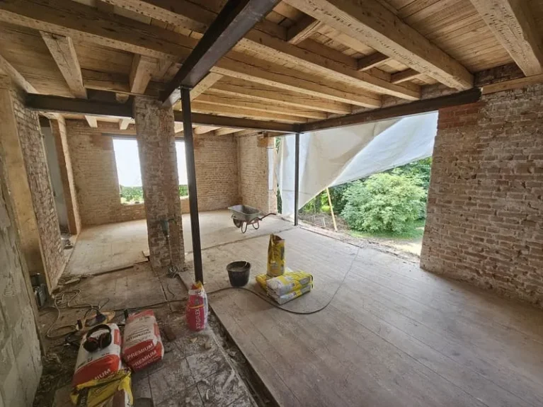 Renovierungsszene: Offener Raum mit Ziegelwänden, Dachbalken, Werkzeug, Baumaterialien und Schubkarre, ideal für Sanierungs- und Baustellen-SEO-Inhalte.