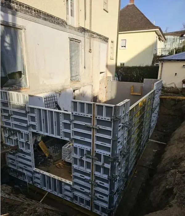 Hausbau: Fundamentarbeiten mit Schalungen, vorbereitet für Beton gießen. Baustelle in urbaner Umgebung, Erdarbeiten sichtbar.