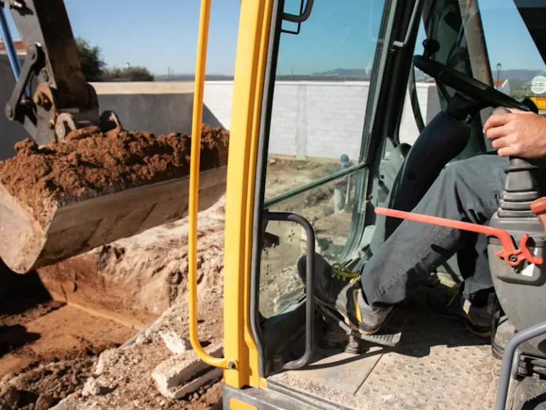 Baggerfahrer bewegt Erde mit Baggerarm auf Baustelle, Innenansicht der Fahrerkabine.