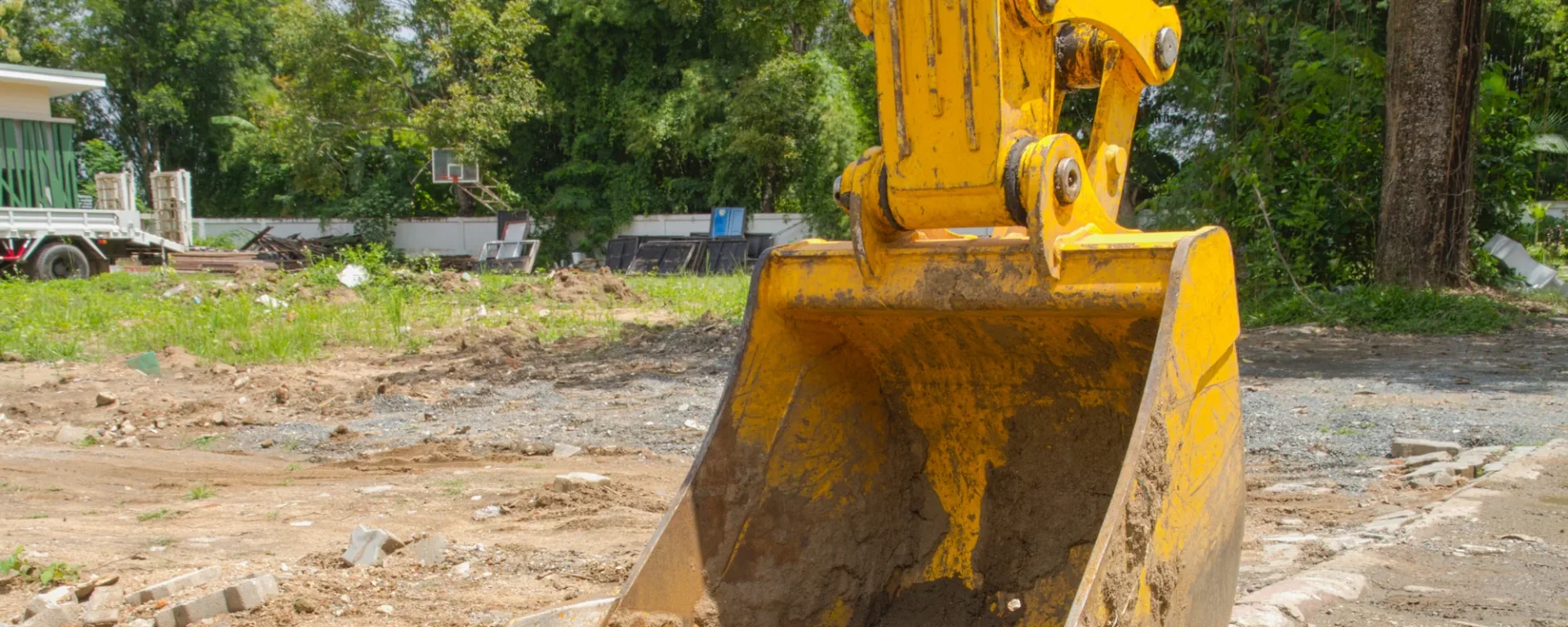 Gelber Bagger auf Baustelle, bereit für Erdarbeiten, im grünen, sonnigen Hintergrund.