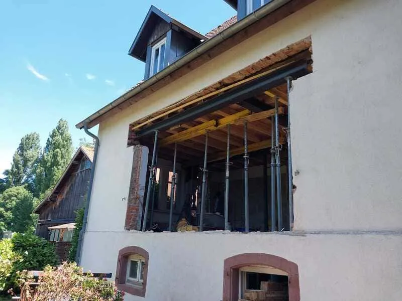 Hausrenovierung: Eine große Wandöffnung mit Stützen, die Bauarbeiten oder eine Erweiterung an einem Wohnhaus zeigt.