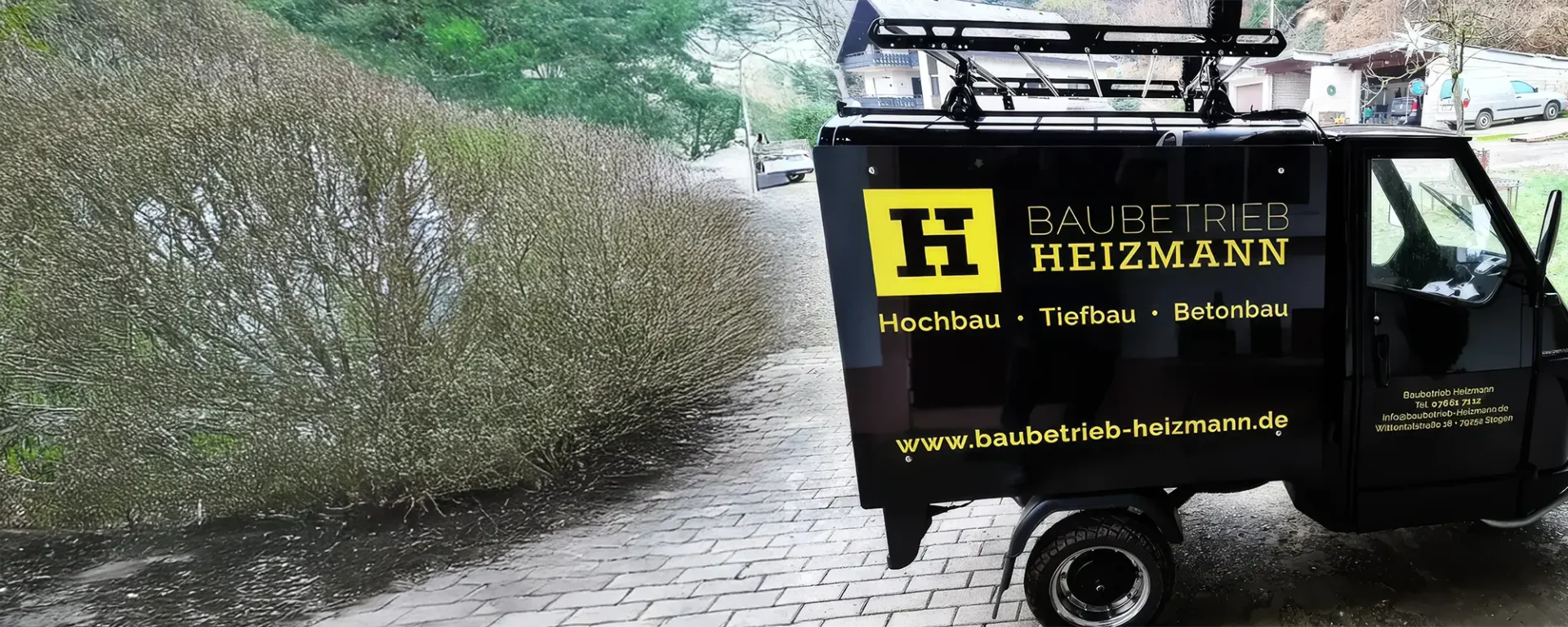 Kleines schwarzes Fahrzeug mit Baubetrieb Heizmann Werbung, spezialisiert auf Hochbau, Tiefbau, Betonbau.